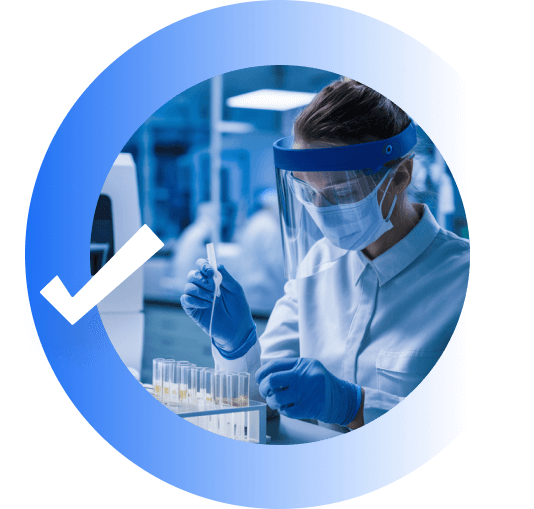 A woman in a laboratory handles test tubes. She is wearing a face mask and shield.