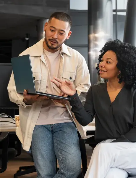 A man holds a laptop as he and a woman look at it together