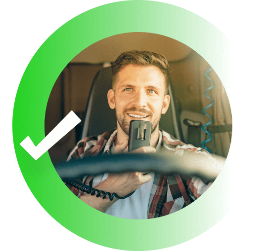 A truck driver smiling and driving while speaking into a microphone