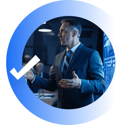 Middle-aged man in a suit presenting data on a large screen in a conference room, shown inside a blue circular graphic with a white checkmark.