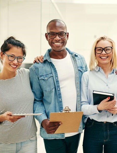 group of smiling colleagues standing together holding clipboards and notebooks