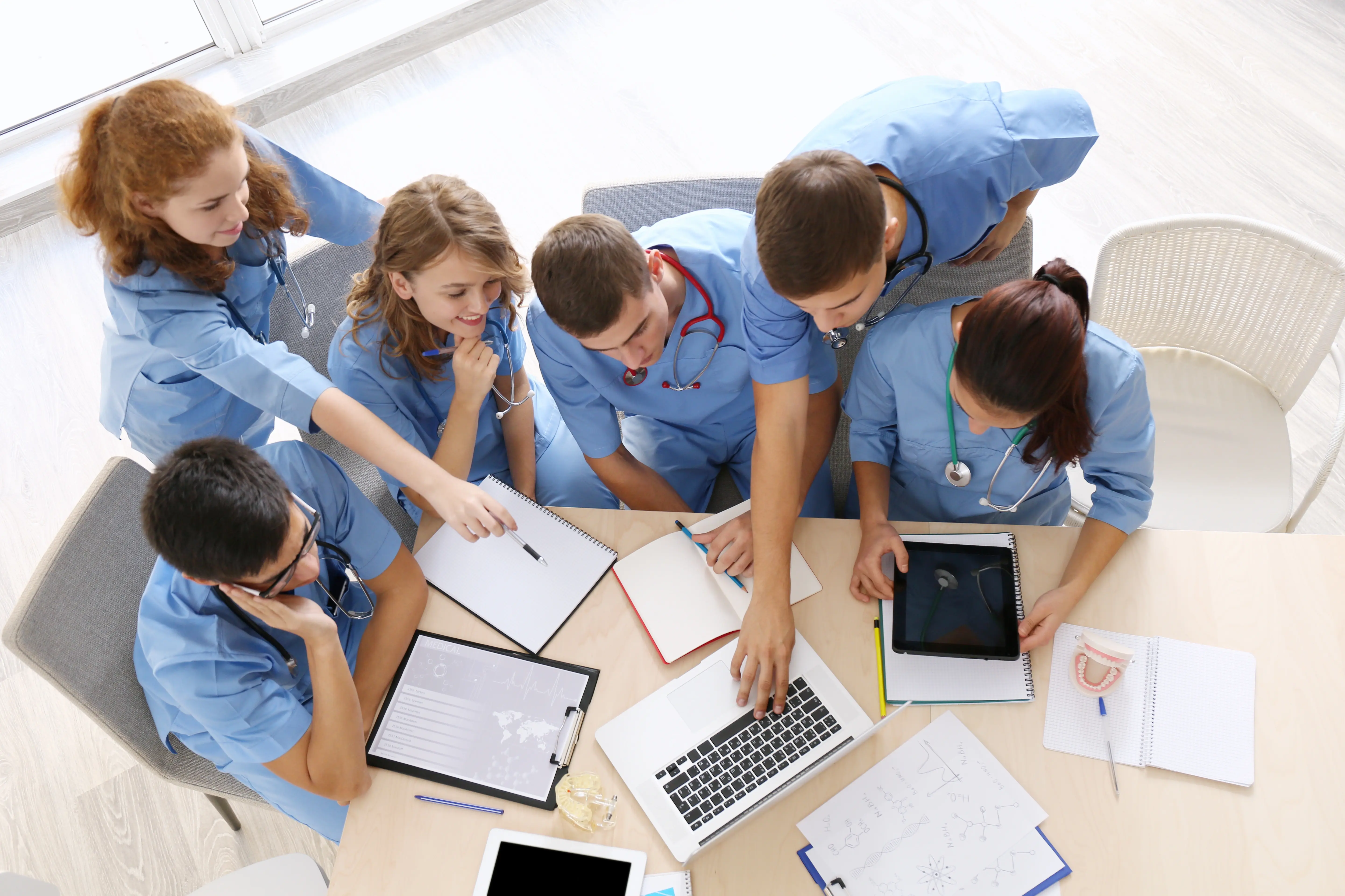 Employees in scrubs working together, gathered around a conference table, viewing documents.